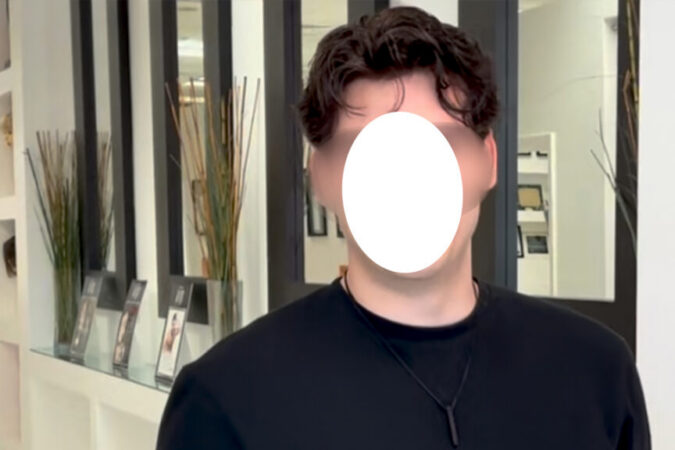 Person in a black shirt standing in a showroom with brochures on a glass shelf; face obscured by a white oval.