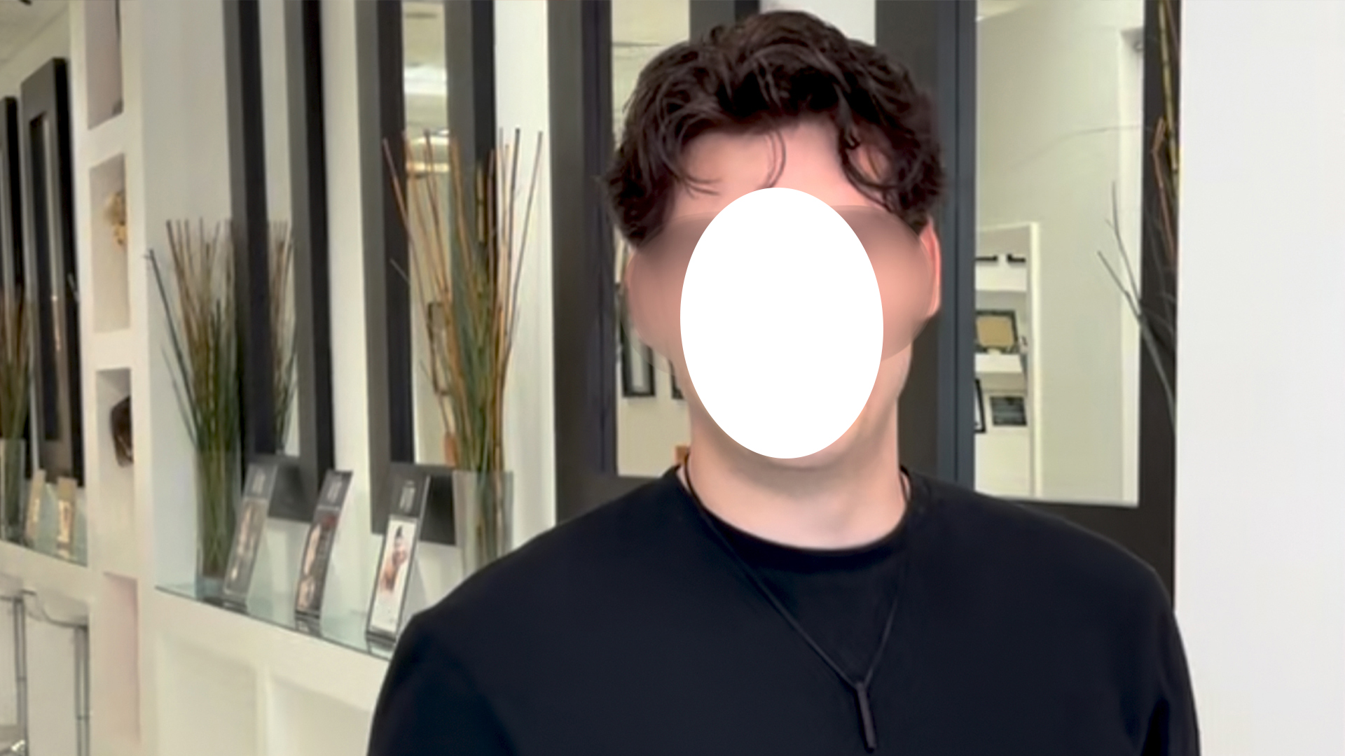 Person in a black shirt standing in a showroom with brochures on a glass shelf; face obscured by a white oval.