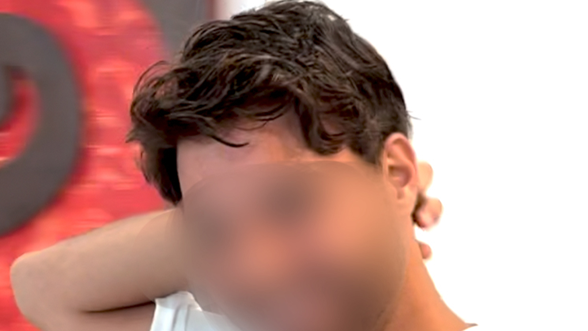 Man with dark hair shielding his face with his arm in a close-up shot.
