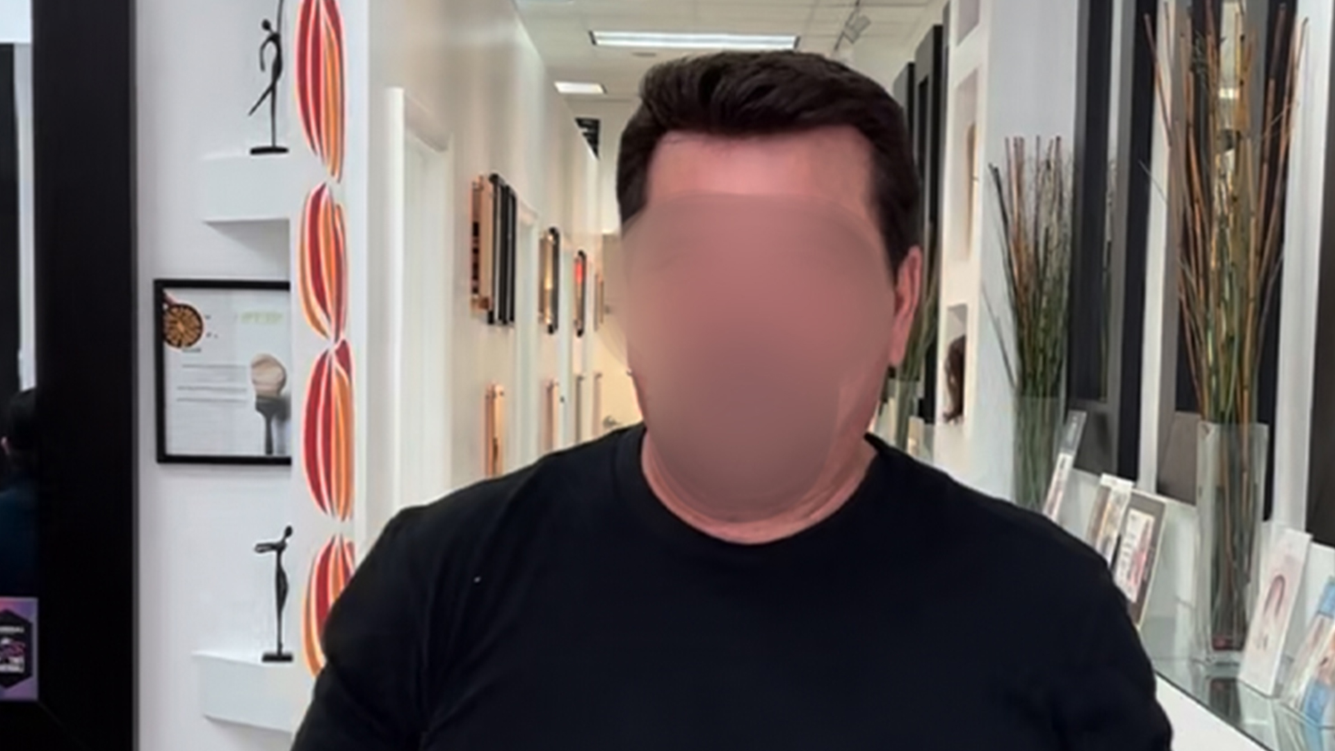 Man in a black shirt stands in a bright showroom with wall art and display shelves along a hallway.